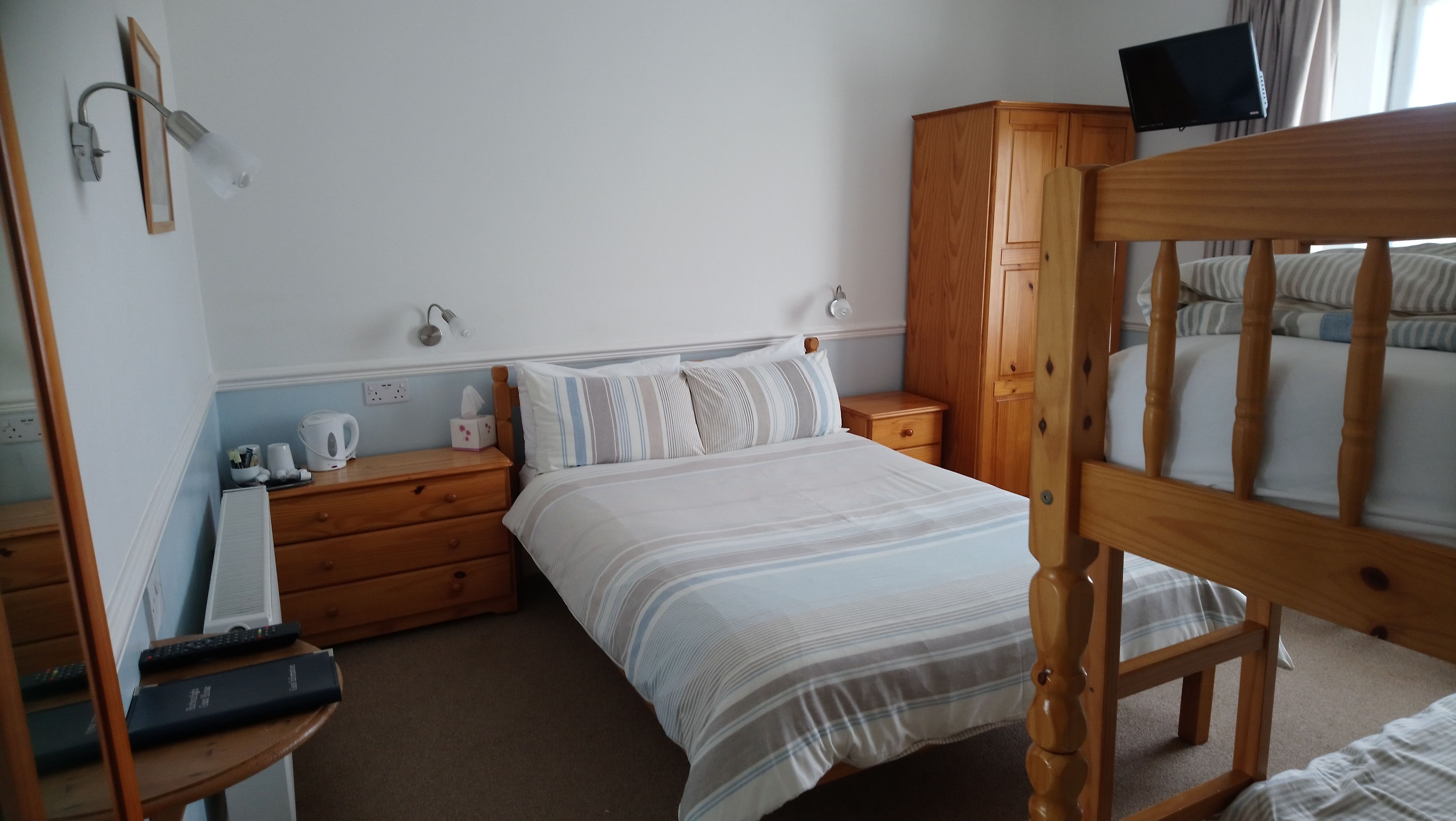 A neatly arranged bedroom with a bed, wooden nightstands, a wardrobe, and a television mounted on the wall.