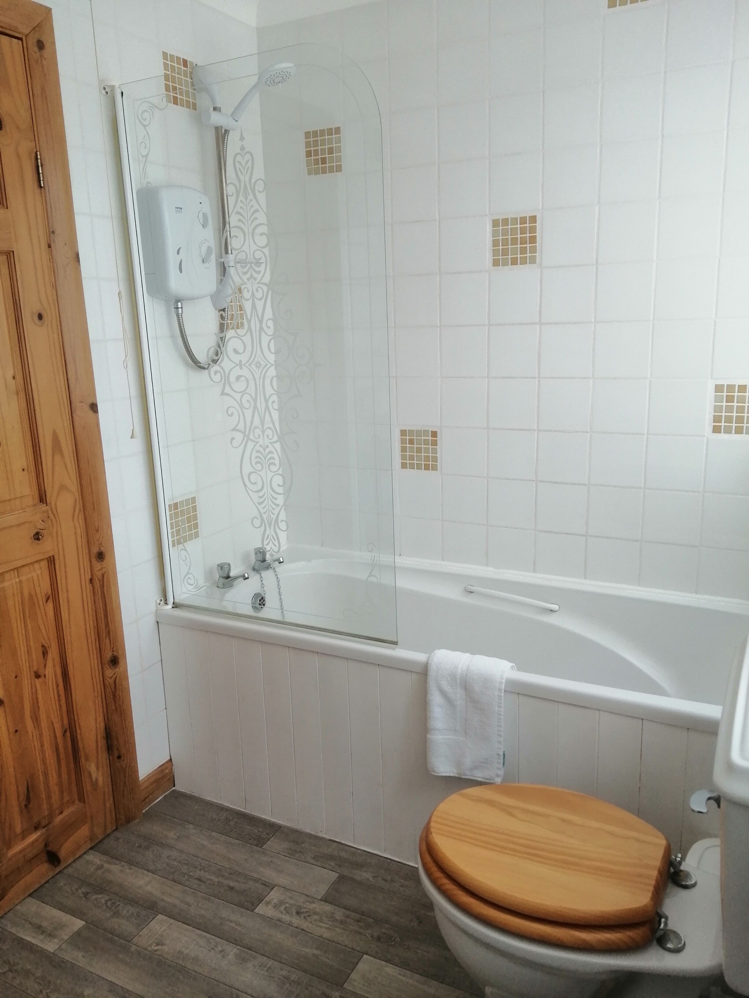 Ein Badezimmer mit Holztür, Duschkabine aus Glas, freistehender Badewanne in Weiß und Toilette mit Holzsitz.