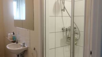 A bathroom with a glass-enclosed shower, a sink with a mirror above it, and a toilet paper holder on the wall.