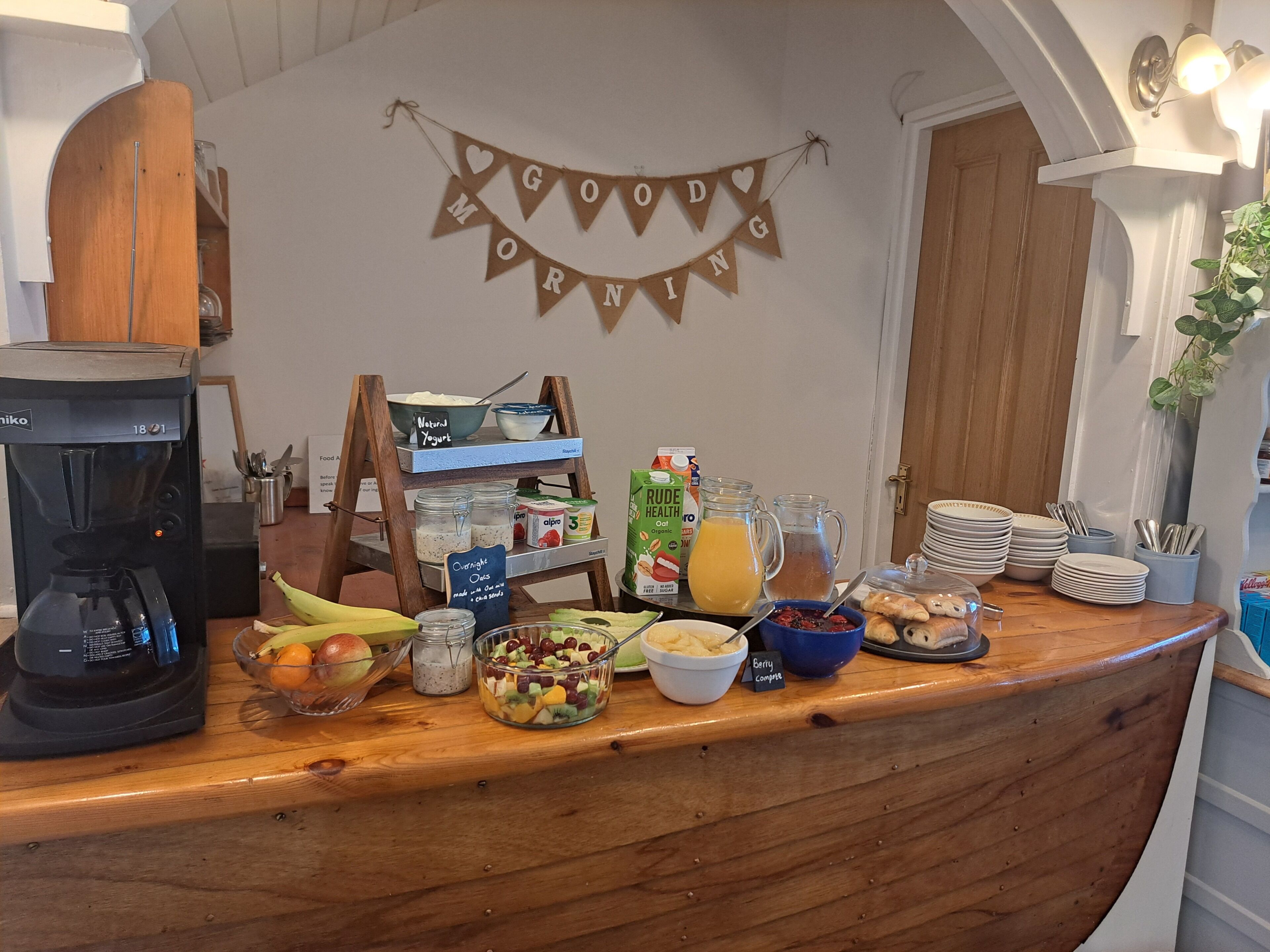 Un buffet de petit-déjeuner avec une machine à café, des saladiers remplis de fruits et une banderole avec l’inscription « Bonjour ».