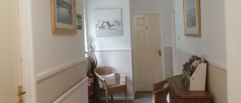 A hallway with a radiator, a wicker chair, a wooden cabinet, and framed pictures on the walls.