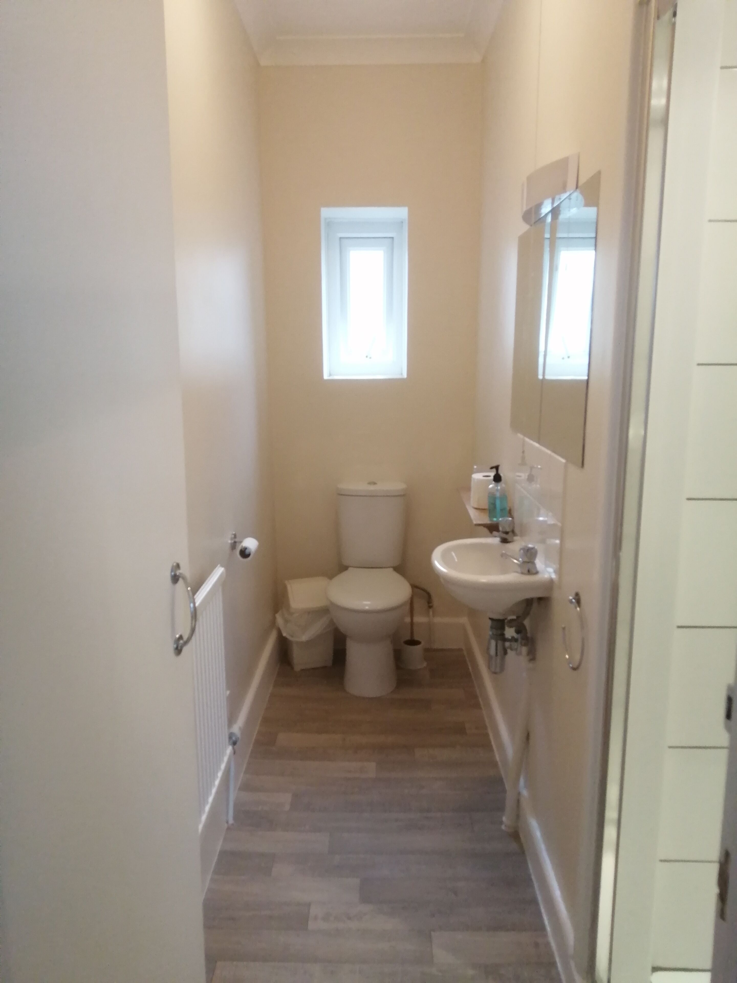 Un baño estrecho con inodoro, lavamanos y un ventanal pequeño.
