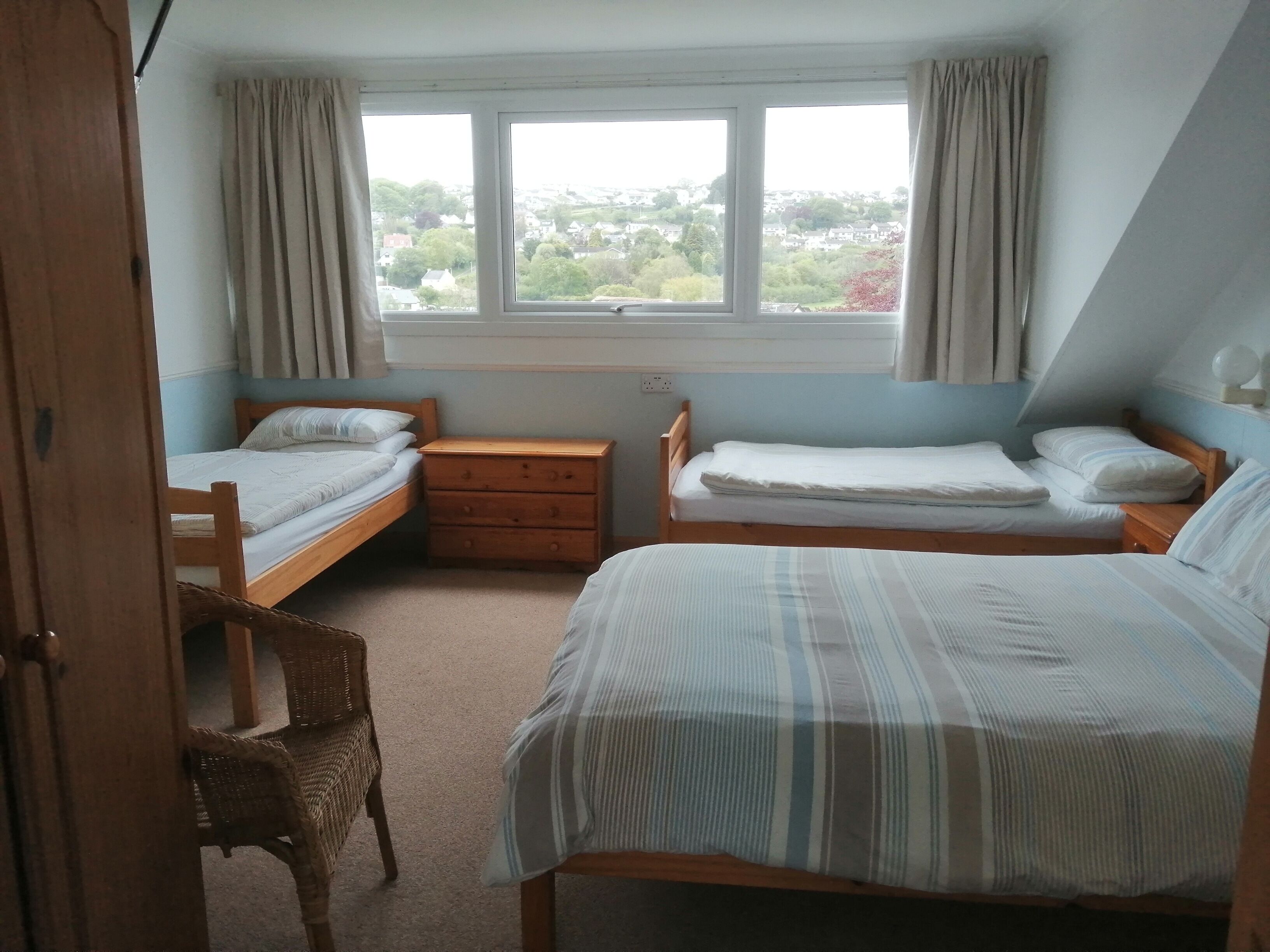 A bedroom with two single beds, a wooden nightstand, a wicker chair, and a window with curtains.