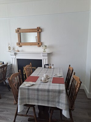 A dining room with a checkered tablecloth, wooden chairs, a fireplace, and a mirror above it. - Harbourlight Guest House (Saundersfoot)