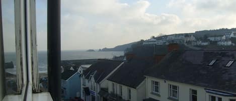 A coastal town with buildings along the waterfront, a clear view of the sea, and a hilly landscape in the background.