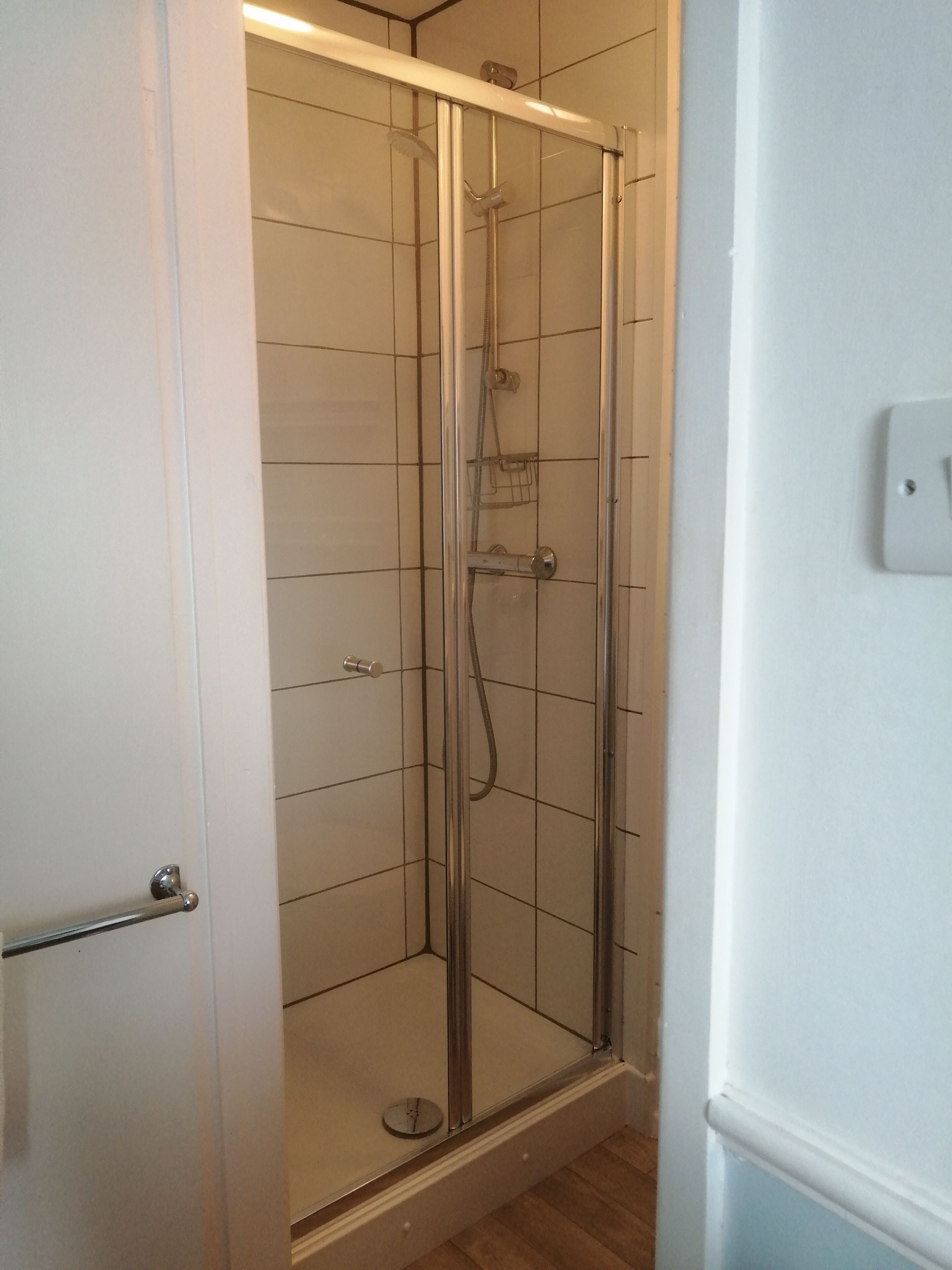Une cabine de douche fermée par des parois en verre, dotée d’un pommeau de douche à main et d’un robinet mural.