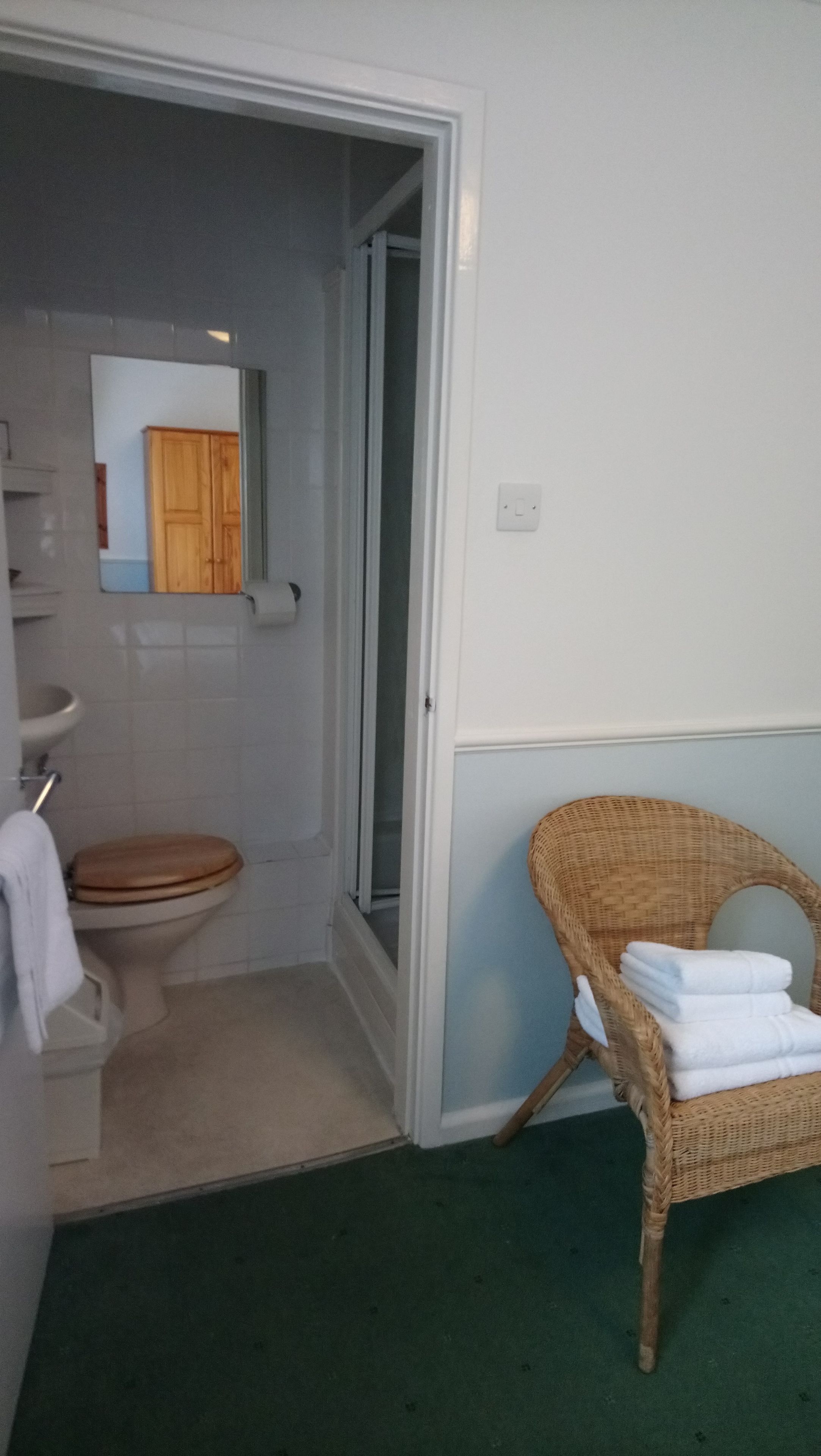 Een badkamer met een toilet, een rieten stoel met handdoeken en een spiegel.