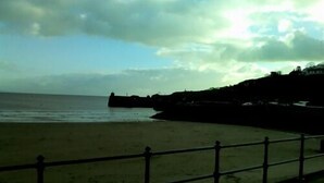 A beach with a wooden fence and a rocky outcrop in the background. - Harbourlight Guest House (Saundersfoot)