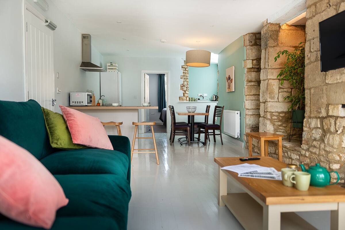 A modern living room with a teal sofa, a wooden coffee table, and a stone wall.