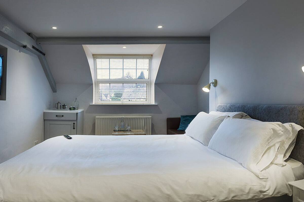 A bedroom with a bed, a TV mounted on the wall, a window, and a radiator.