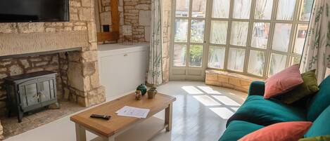 A living room with a stone wall, a flat-screen TV, a wooden coffee table, a green sofa, and a large window with a view.
