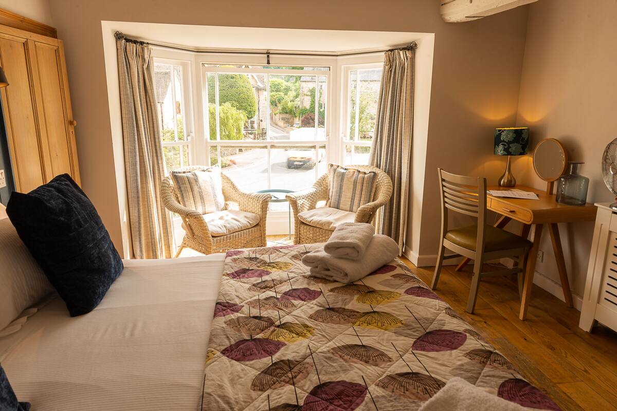A bedroom with a large bed, a desk, a chair, and a view of the outside.