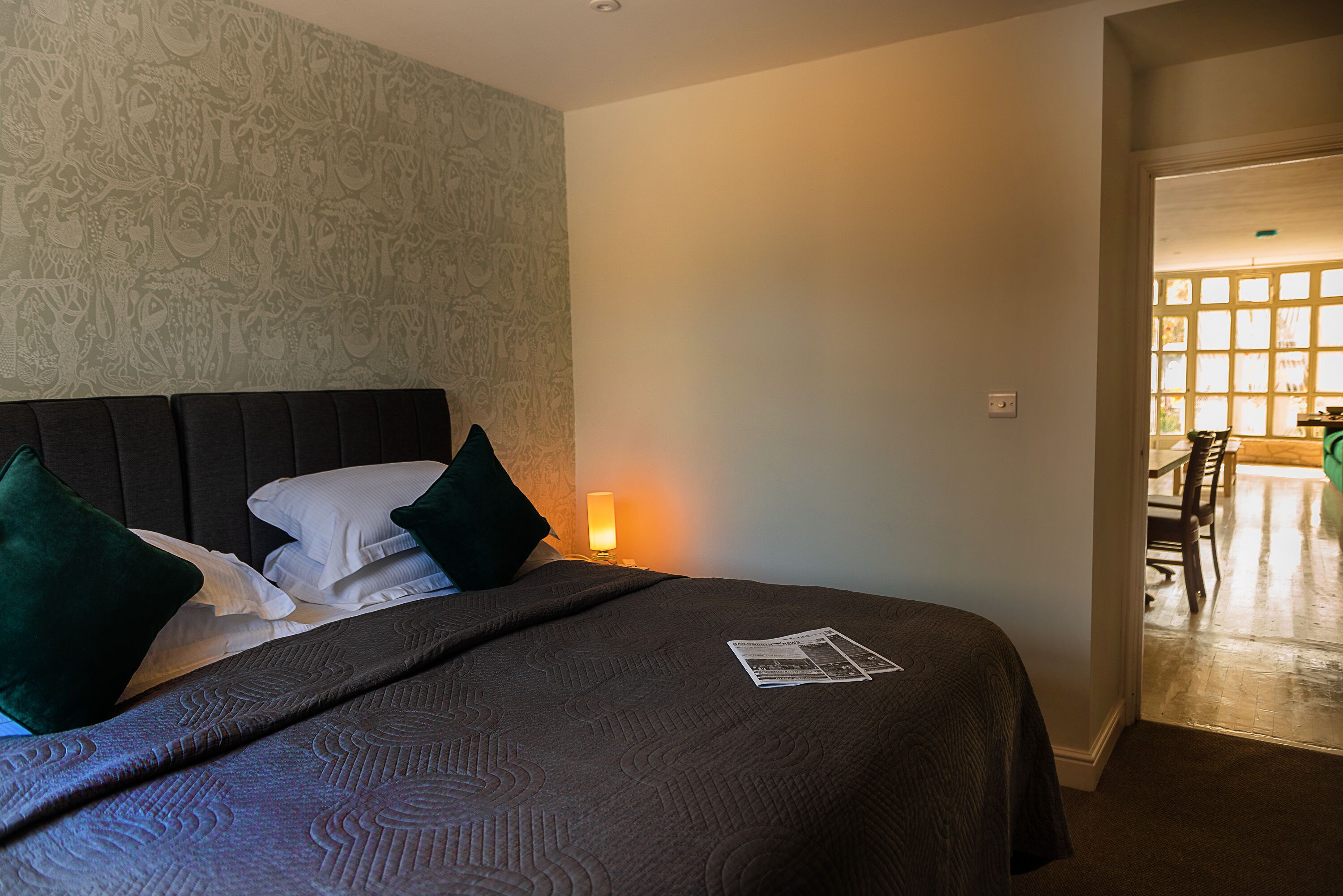 A neatly made bed with a dark headboard, green pillows, and a patterned bedspread.
