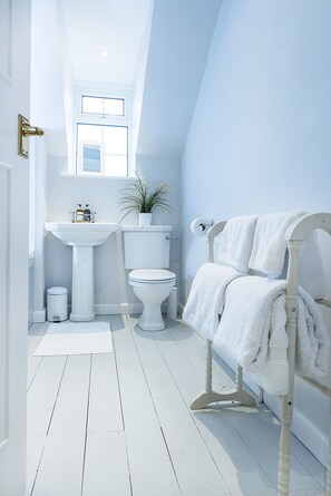 A bathroom with a white sink, toilet, and bathtub, a potted plant, and a towel rack. - Wild Garlic Rooms (Stroud)