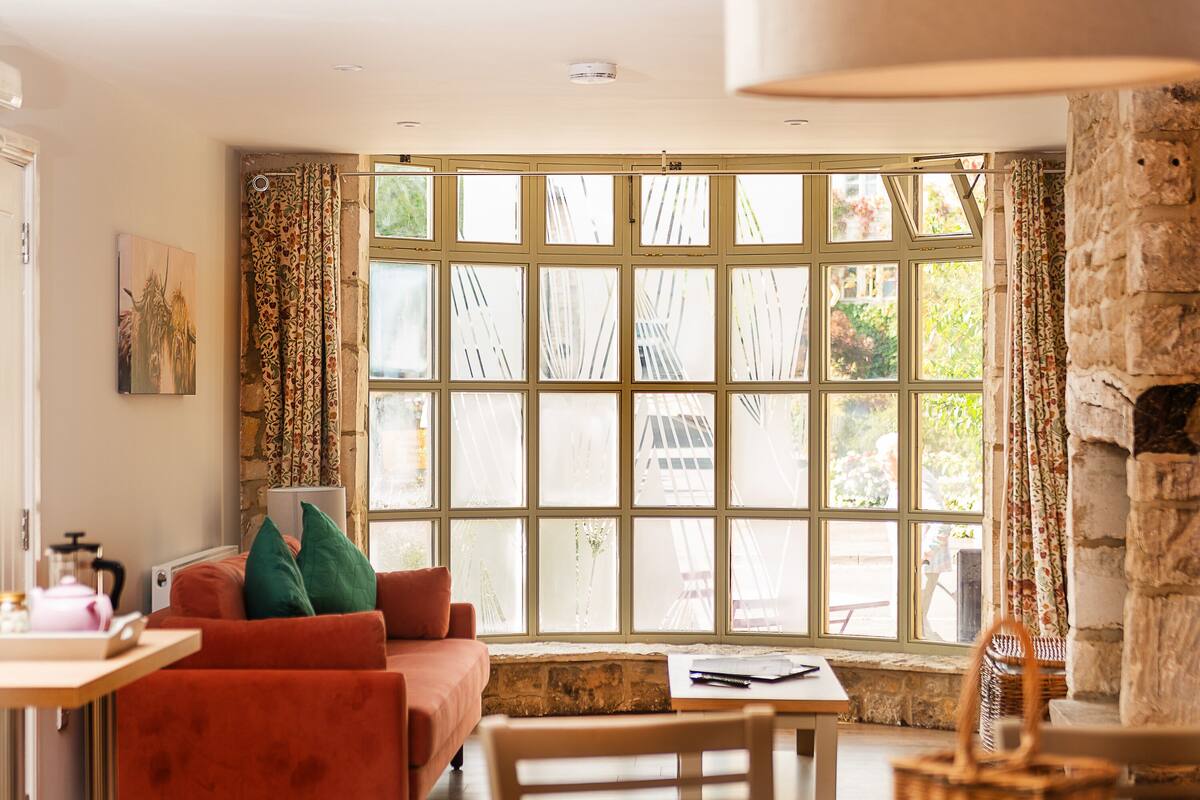 A cozy room with a large window, a sofa, a table, and a chair.