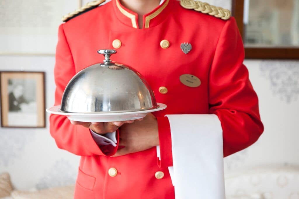 A person in a red uniform holding a silver covered tray.