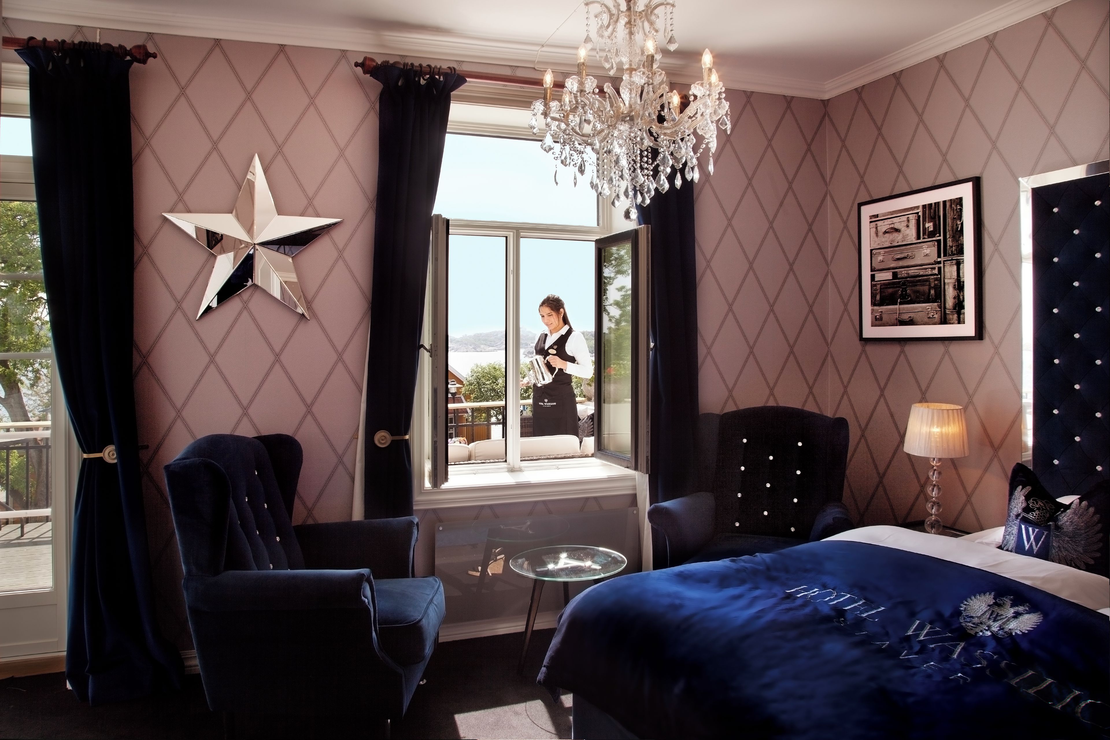 Ein Hotelzimmer mit einem großen Bett, einer Stern-Dekoration an der Wand, einer Chandelüster und Blick ins Freie.