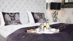 A neatly made bed with a tray of breakfast items, including orange juice, a pitcher, and a cup, in a room with a tufted headboard and patterned wallpaper. - Hotel Wassilioff - Unike Hoteller (Larvik)