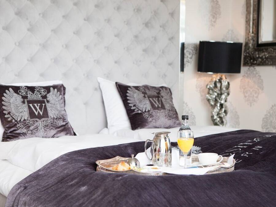 A neatly made bed with a tray of breakfast items, including orange juice, a pitcher, and a cup, in a room with a tufted headboard and patterned wallpaper.