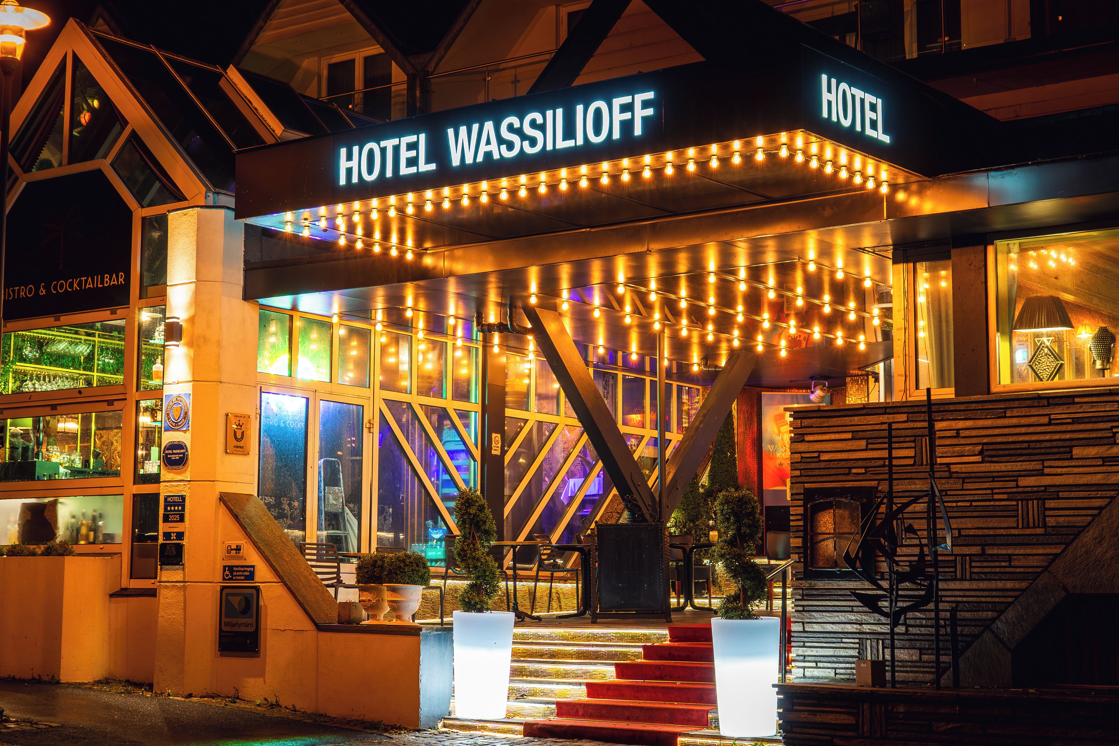 Ein Hotel Eingang mit einem Schild mit der Aufschrift 'HOTEL WASSILIOFF', einem Barbereich und einer Treppe zum Eingang.