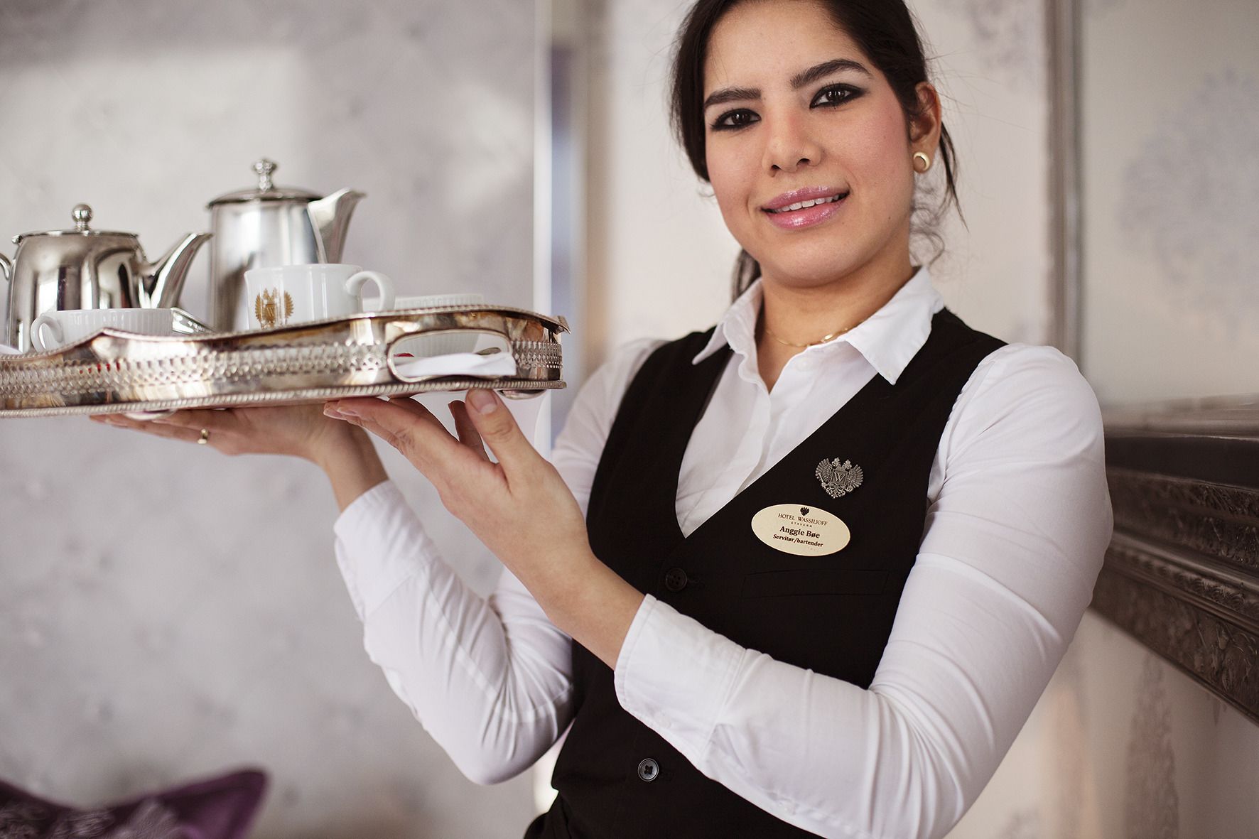 Un empleado de hotel sostiene una bandeja con una tetera y tazas.
