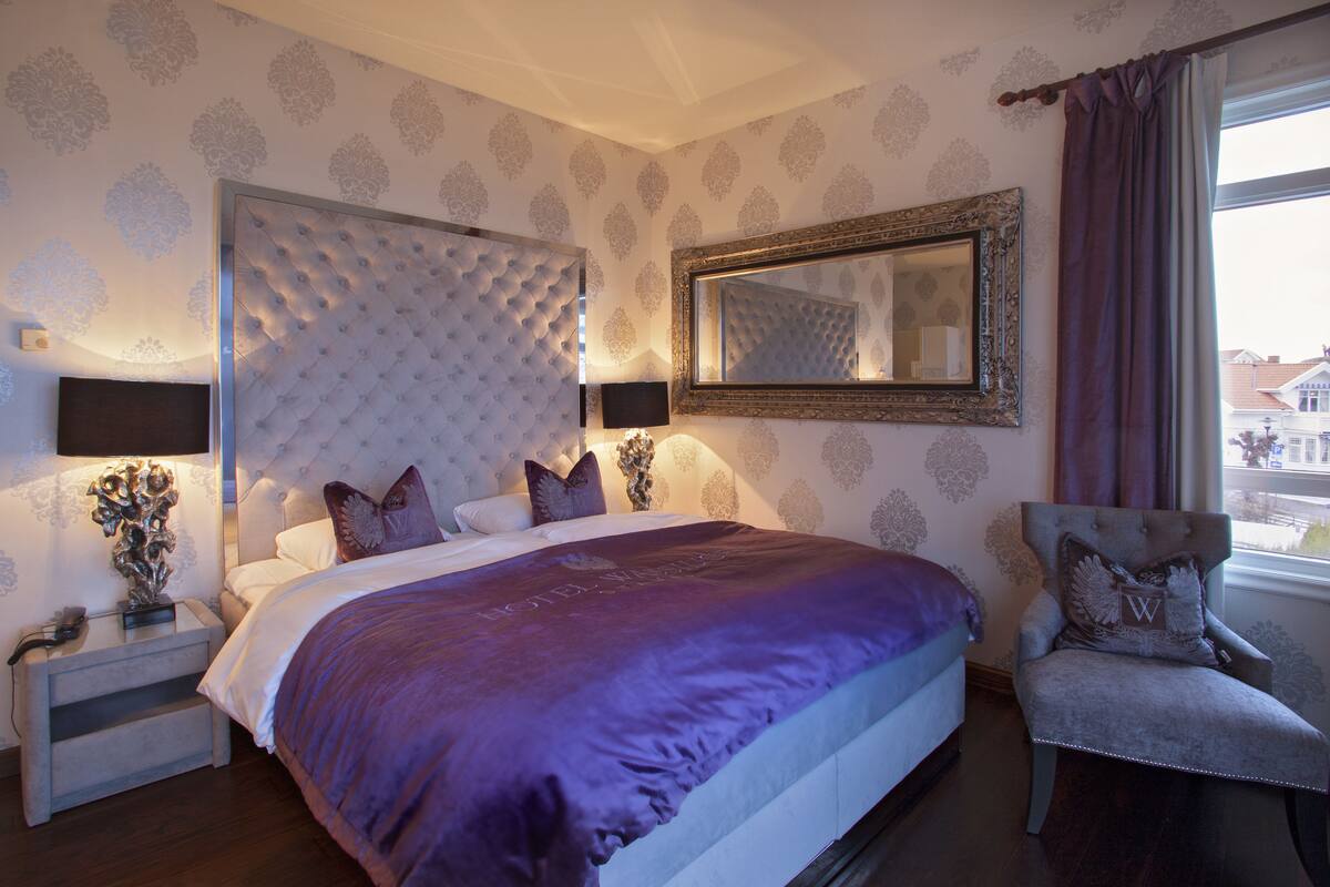 A bedroom with a tufted headboard, a large mirror, and a view of the outside.