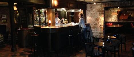 Zona de bar con un bartender y un cliente, paredes de ladrillo y piso a cuadros.