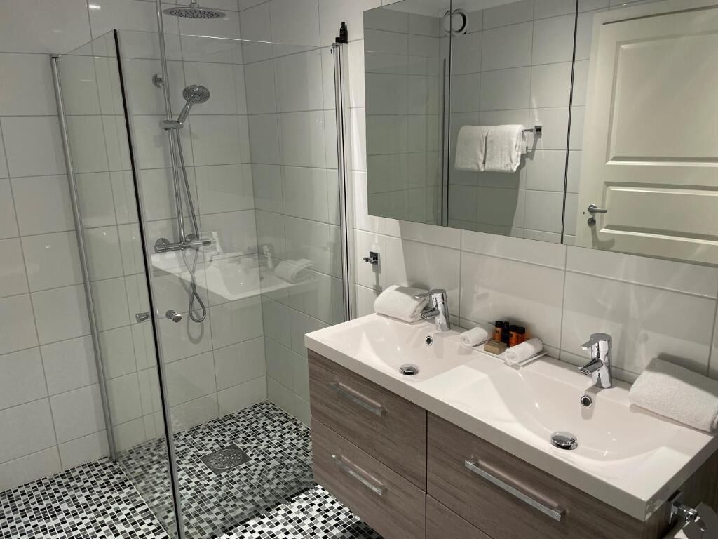 A modern bathroom with a glass-enclosed shower, a vanity with a mirror, and a tiled floor.