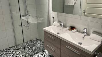 Un baño moderno con ducha de vidrio, tocador con espejo y suelo de baldosas.