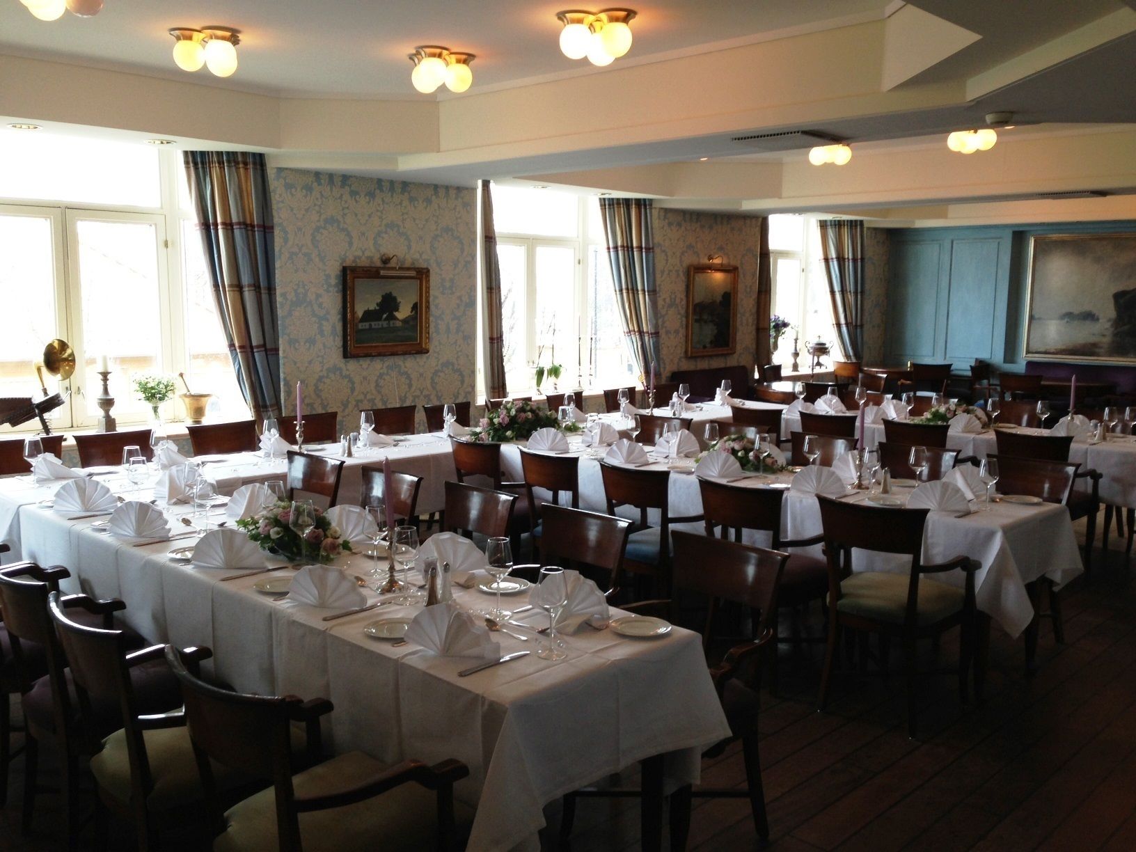 Un comedor formal con varias mesas dispuestas para el servicio, amplias ventanas con cortinas y una decoración de diseño clásico.