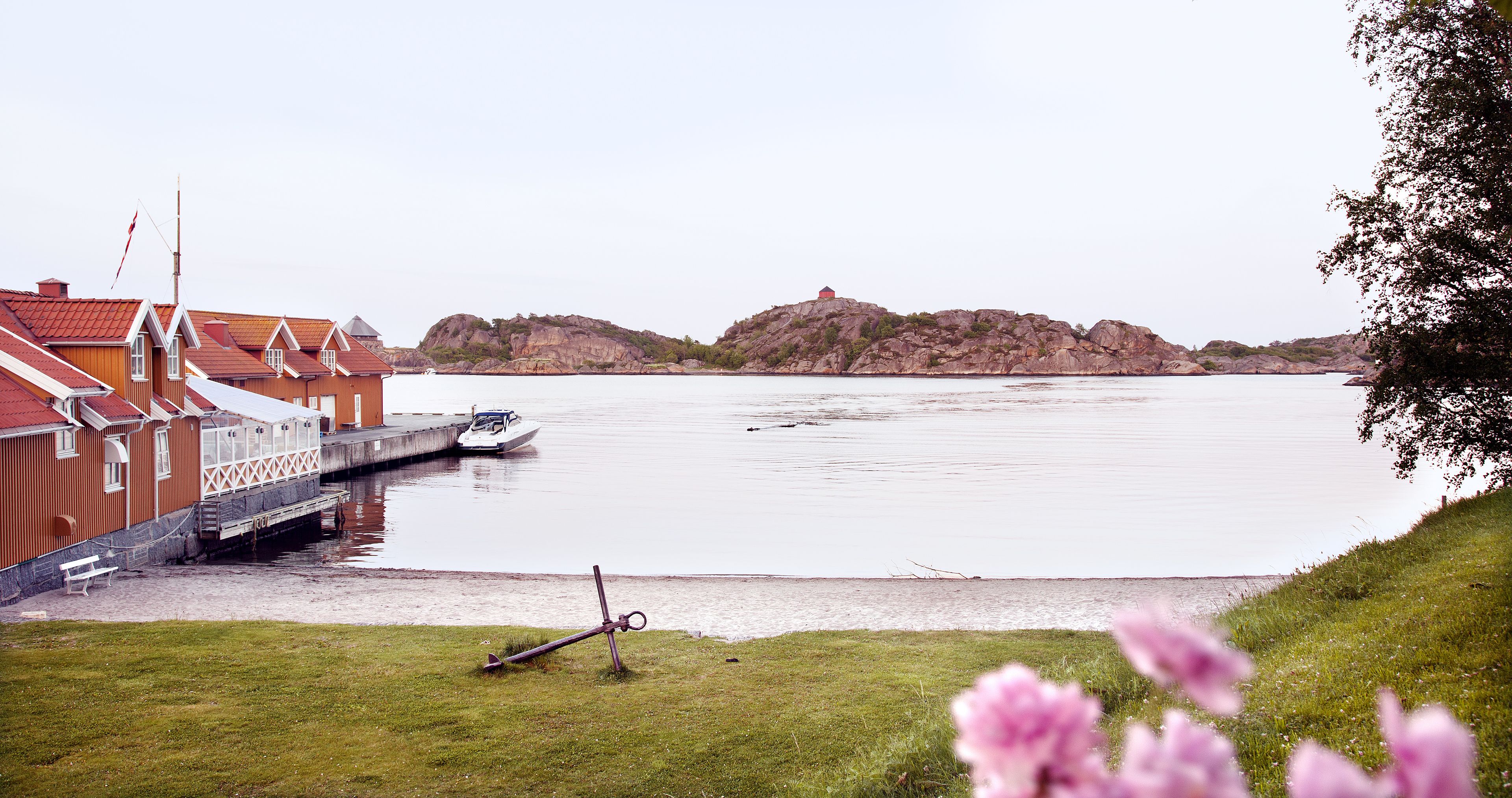 A waterfront property with a dock, a red building with white trim, and a grassy area with flowers.