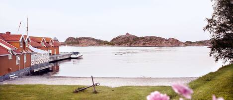 A waterfront property with a dock, a red building with white trim, and a grassy area with flowers.