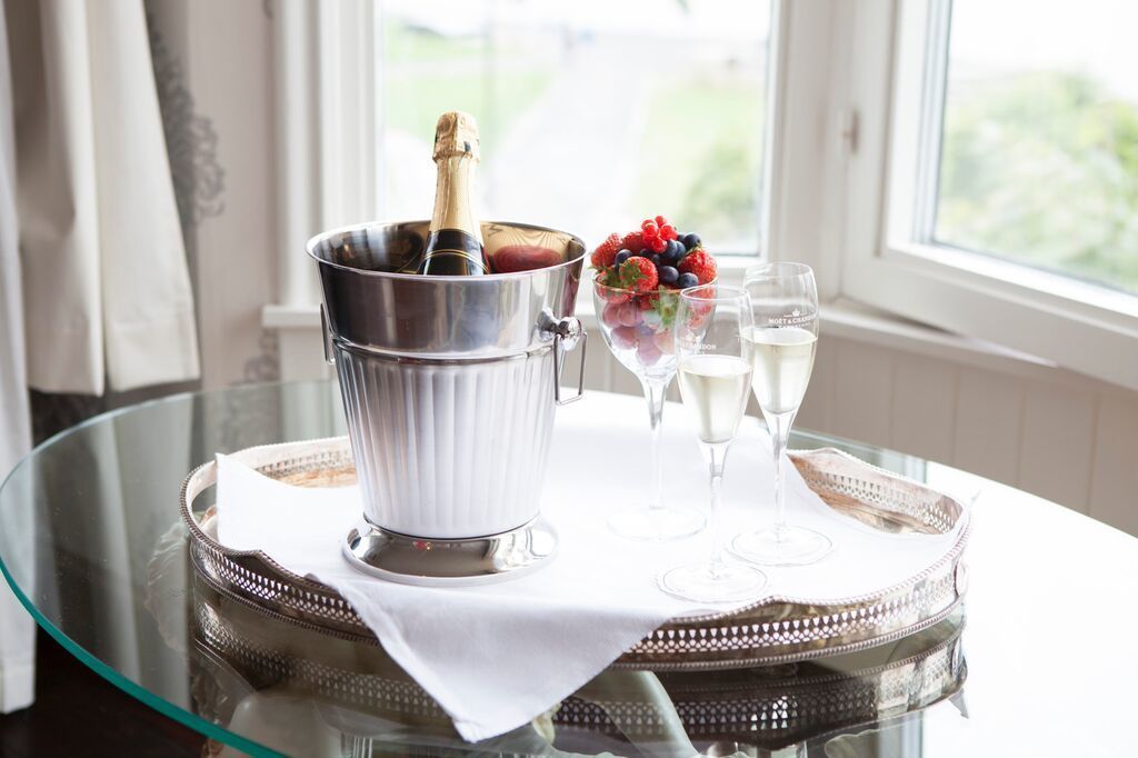 Een glazen tafel met een champagnekoeler, een schaal fruit en twee champagneglazen.