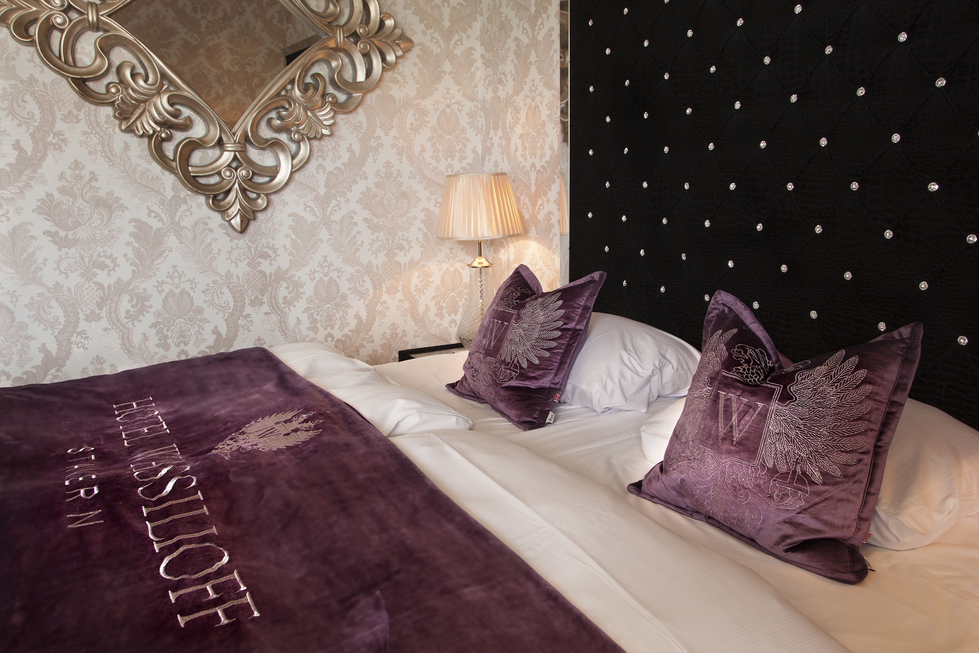 A bedroom with a bed, two pillows, a lamp, and a mirror.