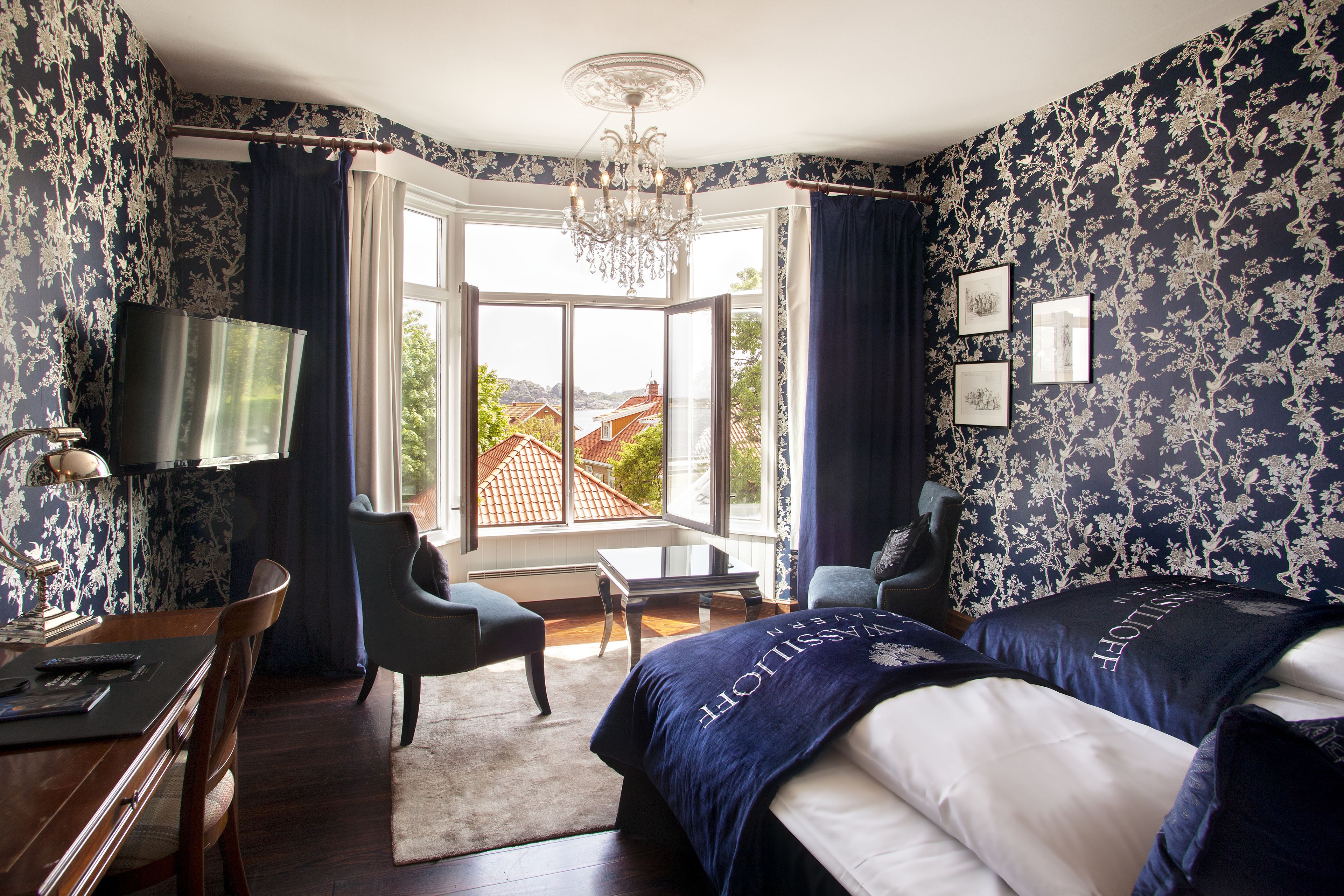 Hotelkamer met een groot bed, twee fauteuils, een bureau met lamp, een televisie en uitzicht op het exterieur.