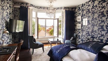 Hotelkamer met een groot bed, twee fauteuils, een bureau met lamp, een televisie en uitzicht op het exterieur.