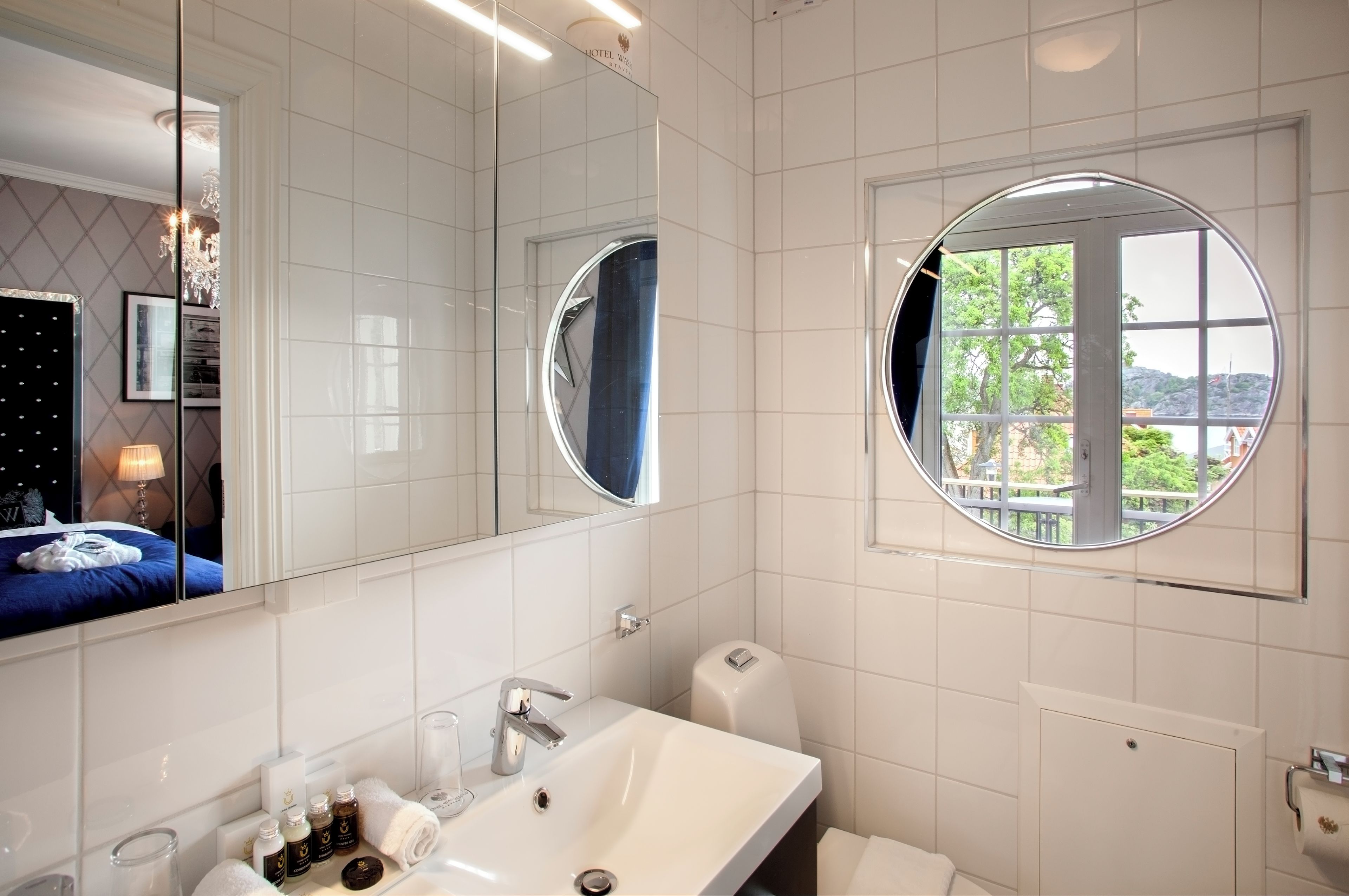 Un baño moderno con un espejo grande, un ventanal redondo y vistas a un balcón.