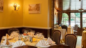 A dining area with tables set for a meal, chairs with patterned upholstery, and a view of greenery through the windows.