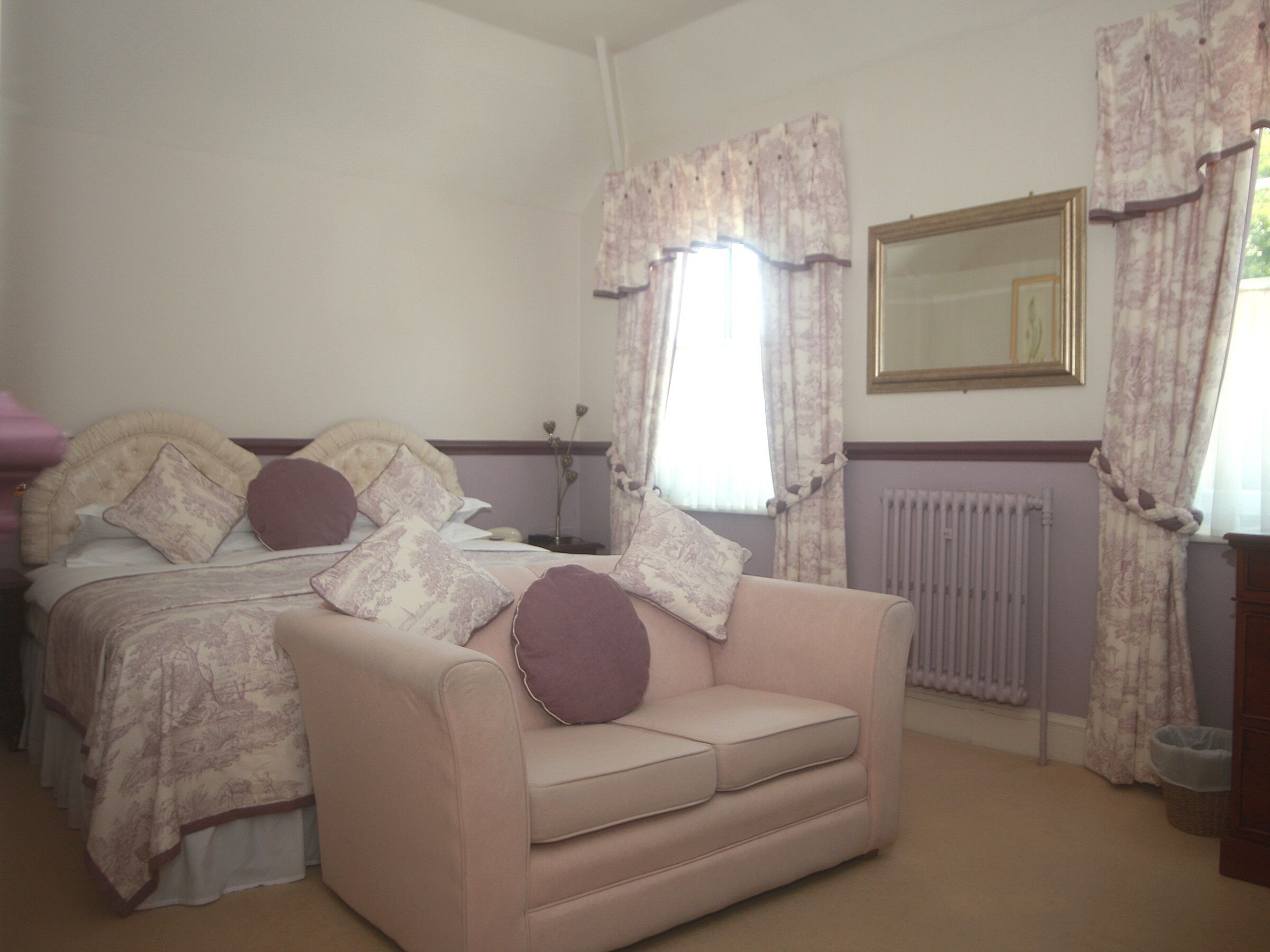A bedroom with a bed, a sofa, a radiator, and a window with curtains.