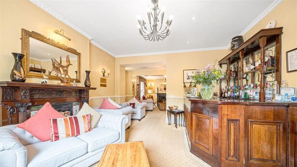 A spacious living room with a bar area, featuring sofas, a wooden coffee table, and a large mirror.