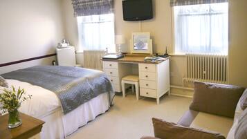 A hotel room with a bed, a desk, a chair, a TV, and a radiator.