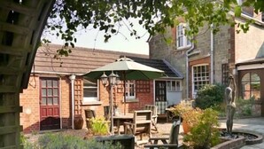 A courtyard with a wooden table and chairs, a green umbrella, and a statue.