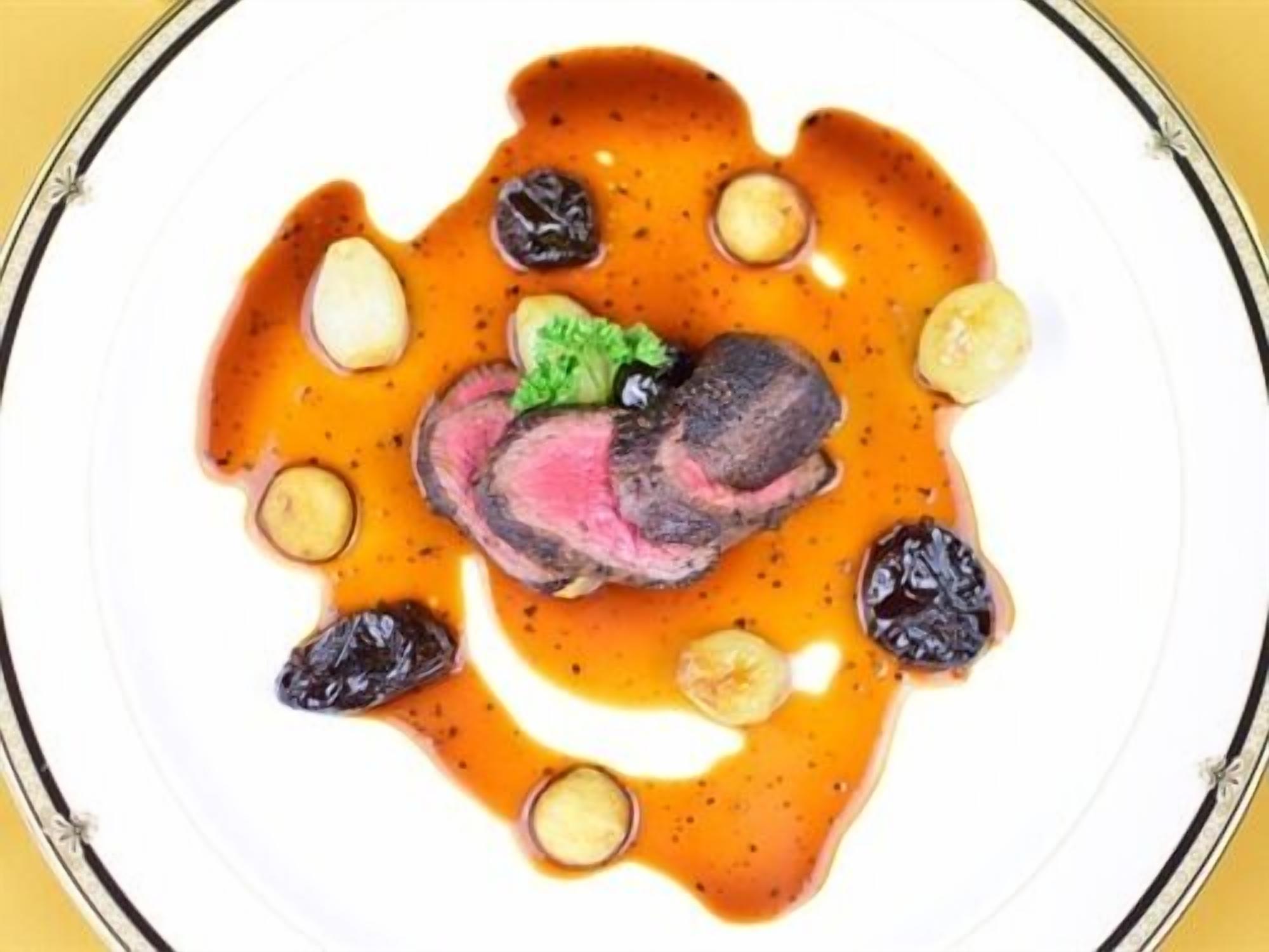 A plate of food with a steak, olives, and a sauce.