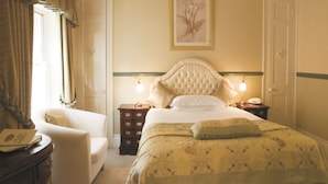 A bedroom with a large bed, a chair, a dresser, and a bedside table with a lamp.