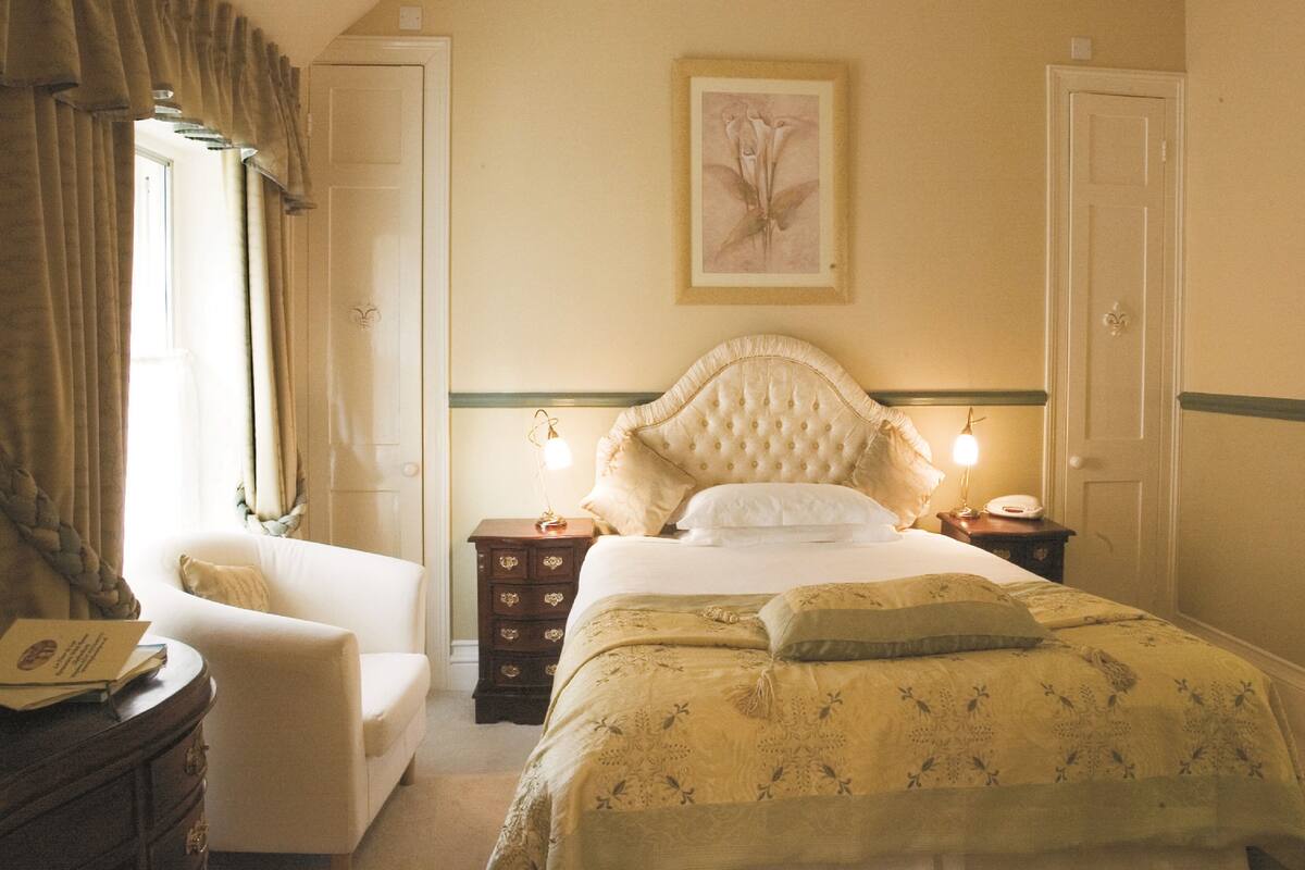 Un dormitorio con una cama grande, una silla, un aparador y una mesita de noche con lámpara.