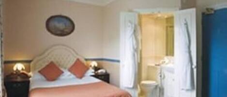 A bedroom with a bed, bedside tables, a nightstand, a mirror, and an open door leading to a bathroom.