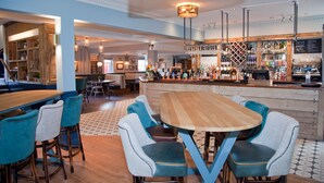 A bar area with a wooden table and teal chairs, a bar counter with various bottles, and a patterned floor.
