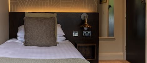 Una cama bien tendida con almohadas y una manta, un aplique de pared y una puerta.