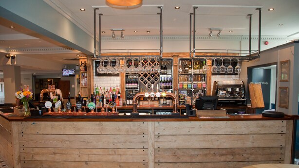 A bar area with wooden counters, a variety of bottles, glasses, and a television screen.