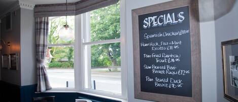 A restaurant interior with a chalkboard menu listing specials, a window with a view of the street, and a round table with chairs.